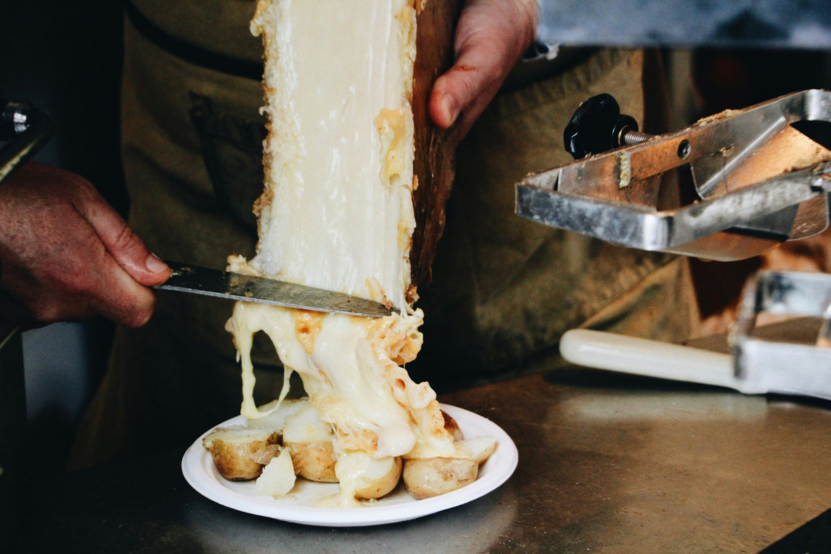 Raclette: Käse wird vom halben Laib auf Kartoffeln geschabt
