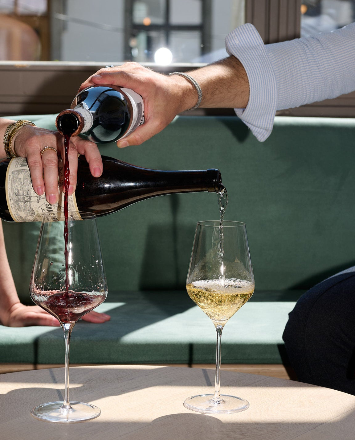 Weiss- und Rotwein werden gleichzeitig aus zwei Flaschen in zwei verschiedene Gläser gegossen.